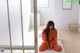 A woman in an orange jumpsuit sitting on a bed.