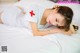 A woman laying on a bed with a red cross on her shirt.