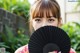 A woman holding a black fan in front of her face.