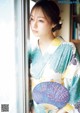 A woman in a kimono holding a fan by a window.