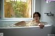 A woman laying in a bathtub in front of a window.